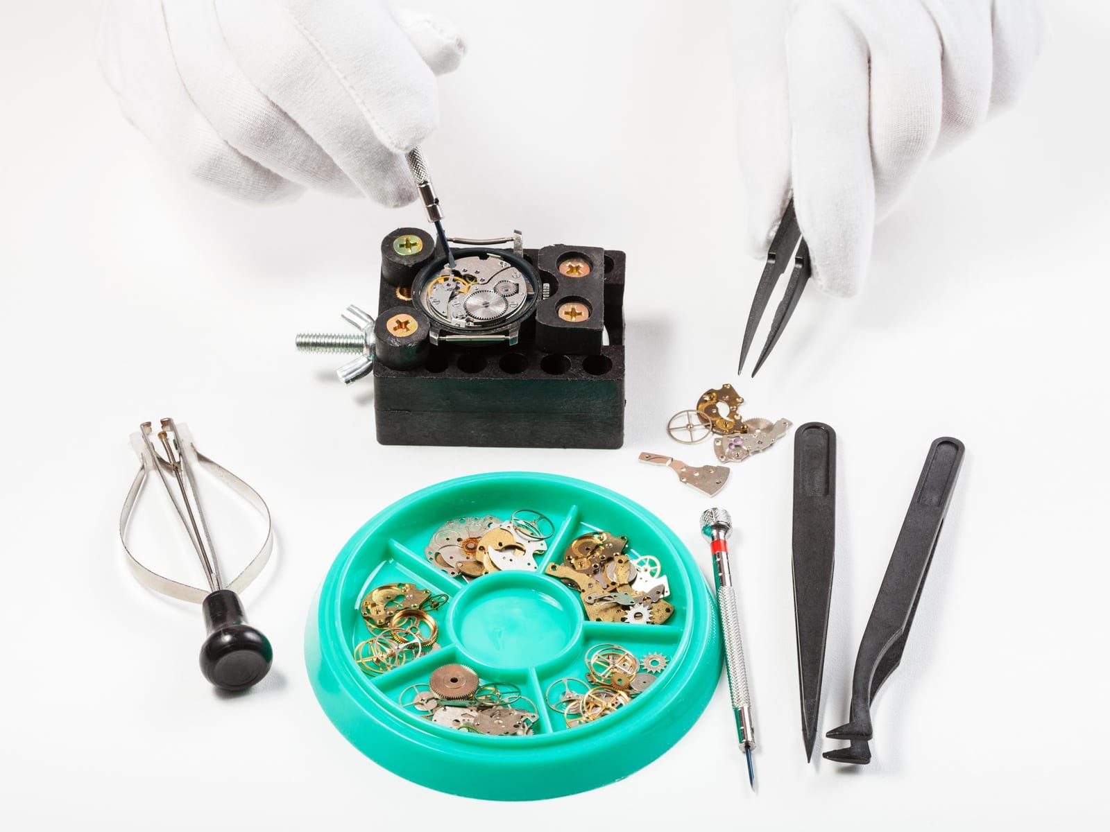 Mani guantate manipolano componenti di un movimento con pinzette e attrezzi da orologiaio